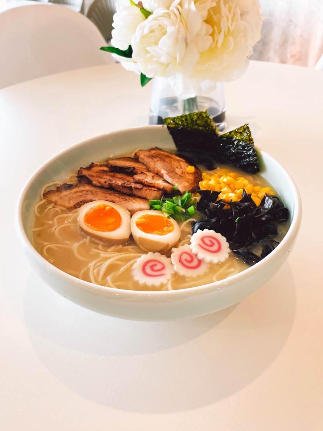 A bowl of creamy-broth ramen with grilled pork, a soft-boiled egg, nori, corn and a pink-swirled fish cake