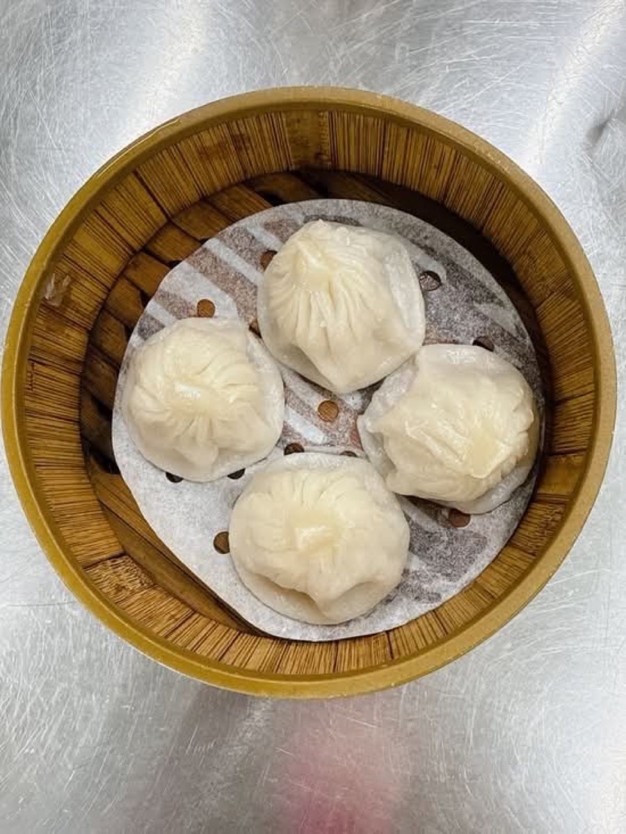 Four xiaolongbao dumplings in a round bamboo steamer lined with paper